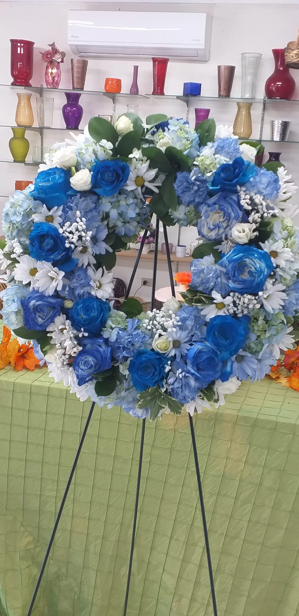 Standing sympathy wreath in blue and white blooms on an easel by Creative Avenues